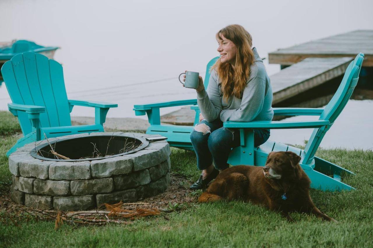 a woman sitting next to a fire pit with a dog at Little Landing Cottage On Cobbossee Lake in Winthrop